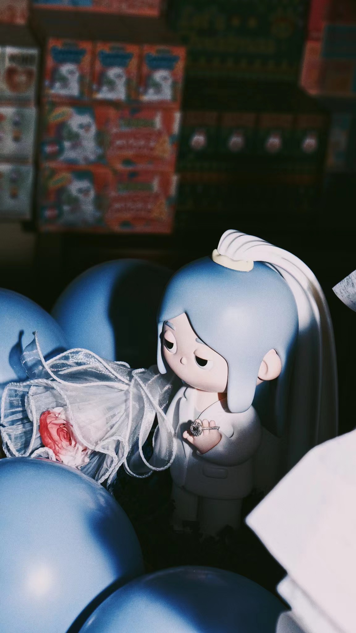 The painted 3D-printed DOU wedding figure holding the proposal ring among blue balloons and flowers